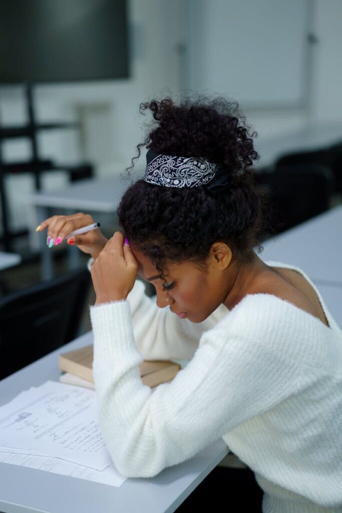 pexels-photo-6209553-6209553 A young woman deeply concentrating while sitting at a desk with study materials.